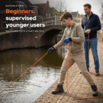 Lifestyle image of a young beginner magnet fishing with adult supervision beside a canal using an orange rope.